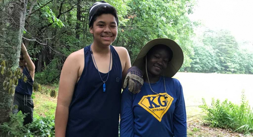 Two people smile in a wooded area. 